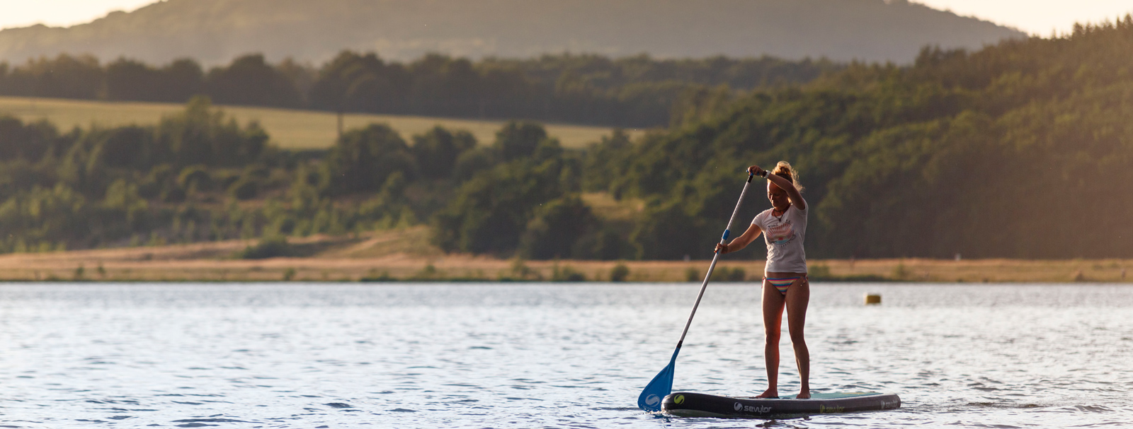 A woman stands on a stand-up paddleboard holding a paddle in her hand.